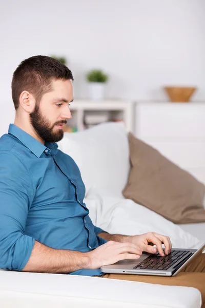 Hombre usando el ordenador portátil mientras está sentado en el sofá —  Fotos de Stock