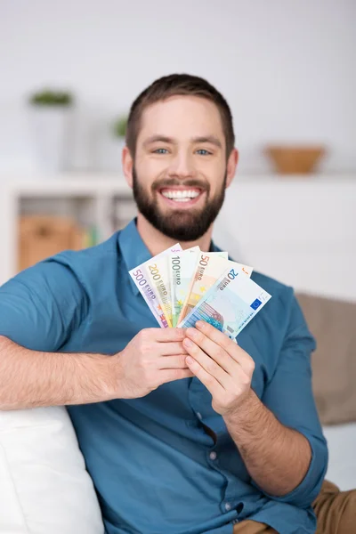 Hombre sosteniendo ventilador de billetes de euro en el sofá —  Fotos de Stock