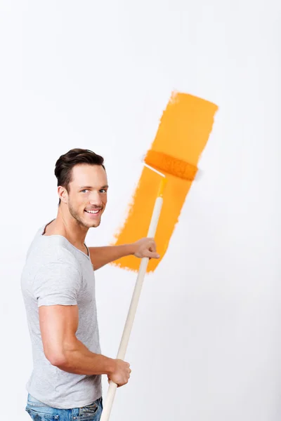 Giovane uomo pittura una parete bianca arancione — Foto Stock