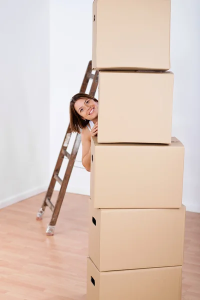 Smiling woman peering from behind stacked boxes — Stock Photo, Image