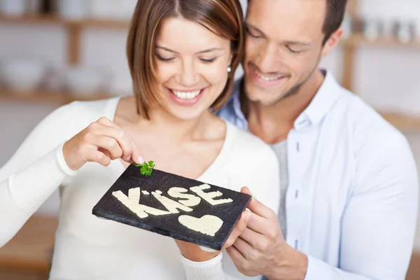 Smiling couple holding a stone slab with cheese — Stock Photo, Image