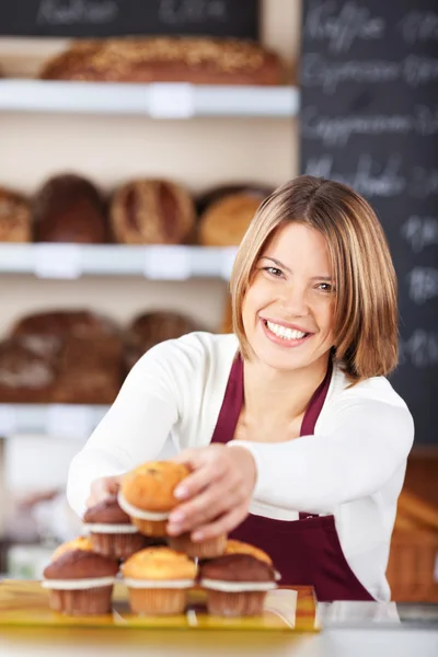 Pretty smiling worker selecting muffins — Stock Photo, Image