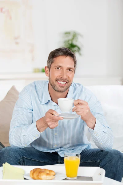 Volwassen man met ontbijt op sofa thuis — Stockfoto