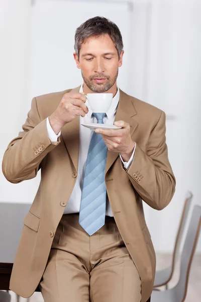 Empresário tomando café enquanto se inclina na mesa — Fotografia de Stock