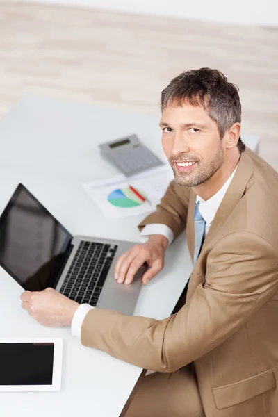 Reifer Geschäftsmann mit Laptop und digitalem Tablet am Schreibtisch — Stockfoto