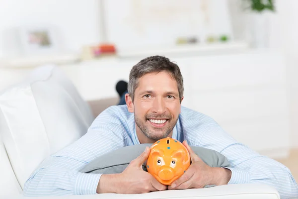 Man med piggybank liggande på soffan — Stockfoto