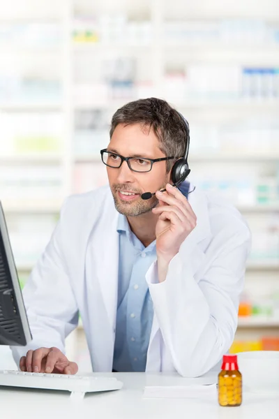 Farmacista che indossa auricolare durante l'utilizzo del computer al bancone — Foto Stock