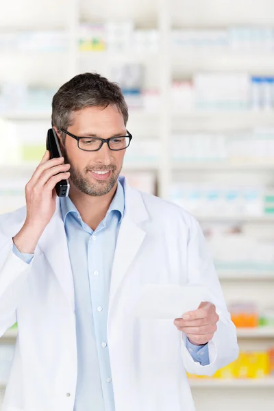 Pharmacist Using Phone While Reading Prescription At Counter — Stock Photo, Image