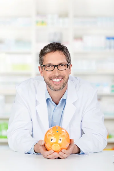 Farmacista maschio che tiene il salvadanaio al banco della farmacia — Foto Stock