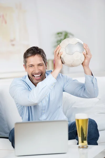 Hombre con balón de fútbol y cerveza viendo partido en el ordenador portátil — Foto de Stock