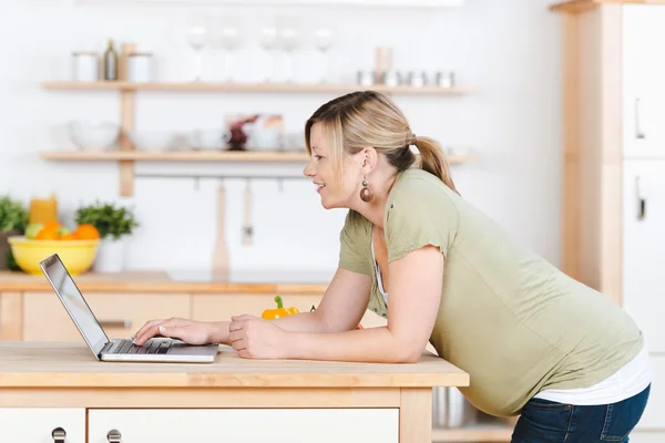 Donna incinta che utilizza il computer portatile mentre si appoggia sul bancone della cucina — Foto Stock