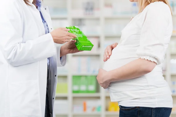 Farmacéutica mostrando producto a mujer embarazada en farmacia —  Fotos de Stock