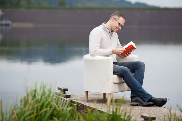 Man läser bok medan du sitter på piren — Stockfoto