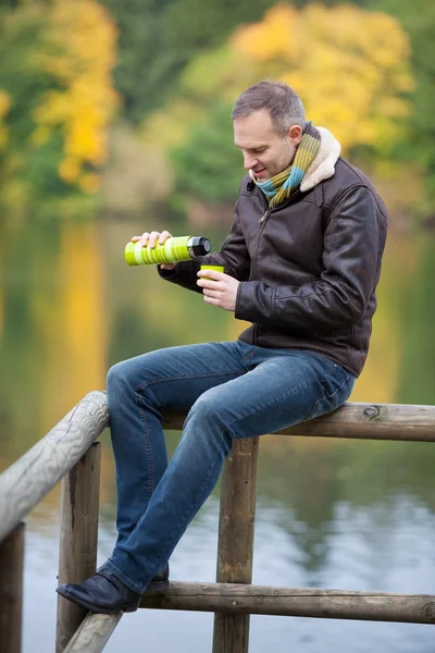 Man Pouring Coffee From Thermos While Sitting On Fence — Stock Photo, Image