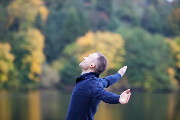 Uomo sorridente con le braccia tese contro il lago — Foto Stock