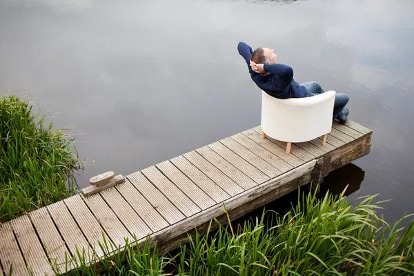 Człowiek z rękami za głowę relaks na fotelu na molo — Zdjęcie stockowe