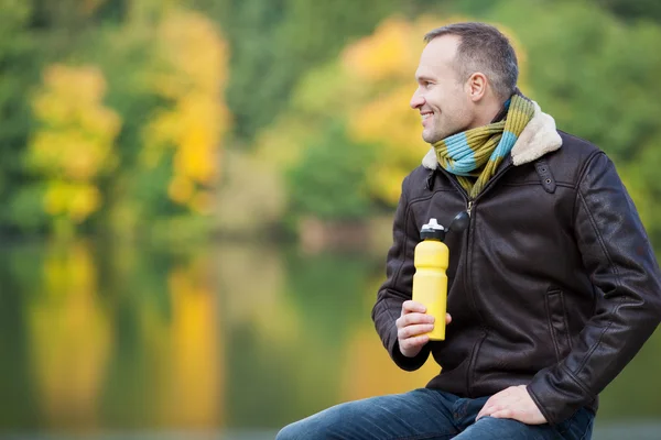Man Holding Water Bottle While Looking Away Against Lake — Stock Photo, Image