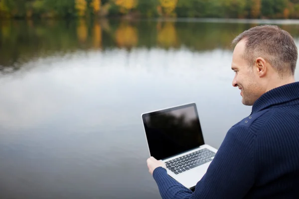 Homem usando laptop com lago no fundo — Fotografia de Stock