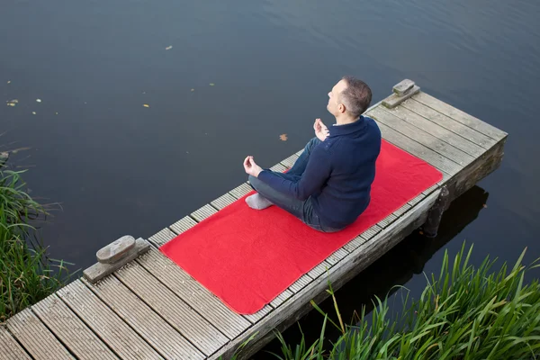 Homem meditando na posição de lótus no cais — Fotografia de Stock