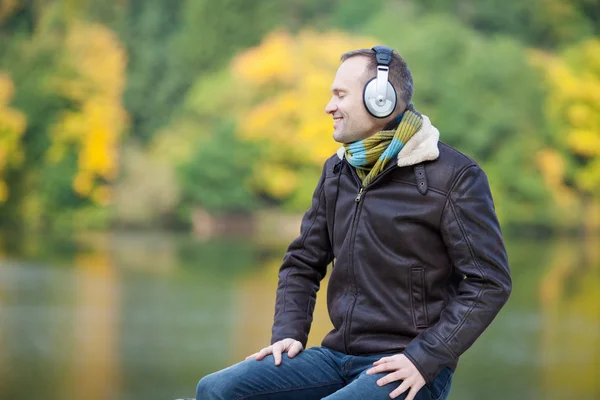 Uomo ascolto di musica su cuffie con lago in background — Foto Stock