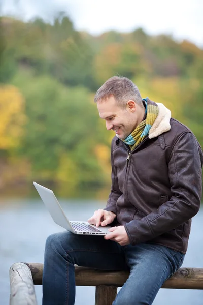 Homem usando laptop enquanto sentado em cerca — Fotografia de Stock