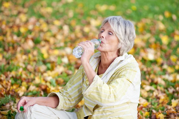 Seniorin trinkt Wasser im Park — Stockfoto