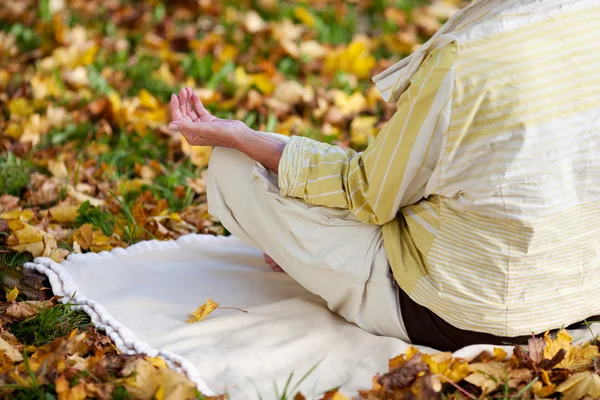 Starší žena přemýšlí v lotosové pozici v parku — Stock fotografie