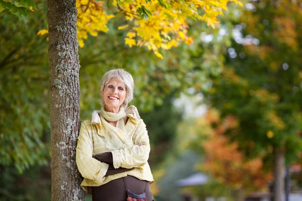 Park ağaç gövdesi üzerine eğilerek gülümseyen kadın kıdemli — Stok fotoğraf
