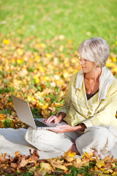 Äldre kvinna med laptop medan du sitter i park — Stockfoto