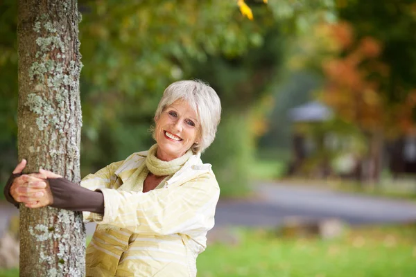 Femme âgée tenant le tronc d'arbre dans le parc — Photo