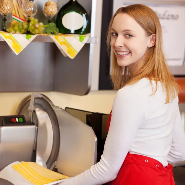 Verkäuferin hält Schnittkäse, während sie gegen Maschine steht — Stockfoto