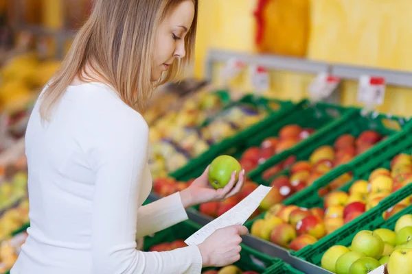 Vrouw met apple tijdens het lezen van de checklist in supermarkt — Stockfoto