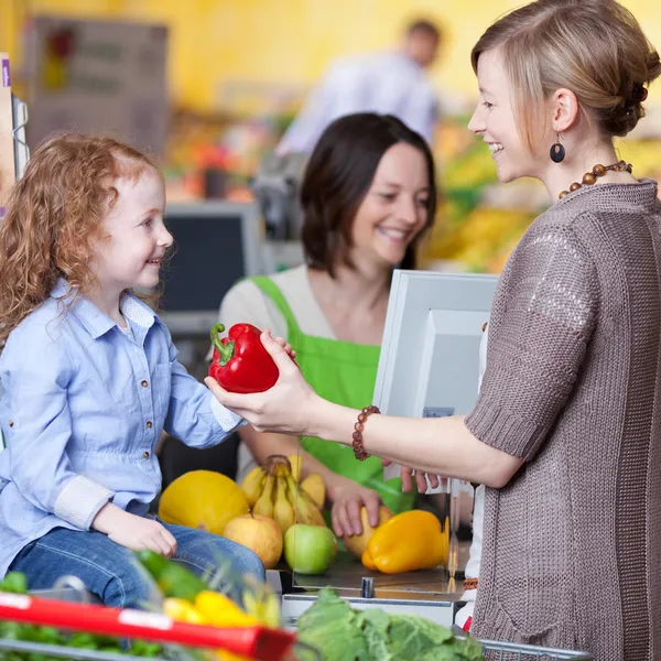 Kobieta podając papryka córkę na licznik z kasą w supermarkecie — Zdjęcie stockowe