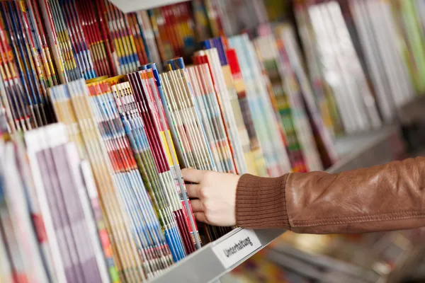 Vrouw handen kiezen tijdschriften van plank — Stockfoto