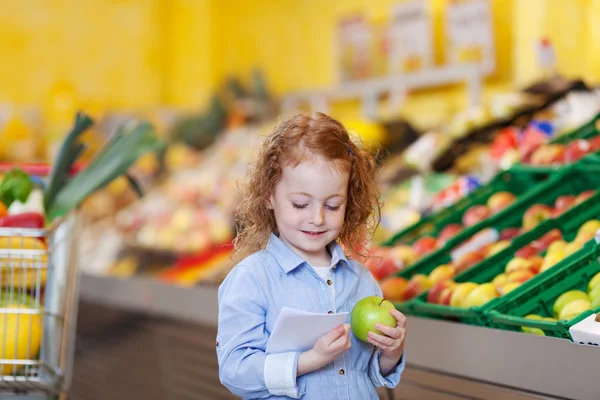 Mädchen liest Checkliste, während sie im Supermarkt einen Apfel hält — Stockfoto