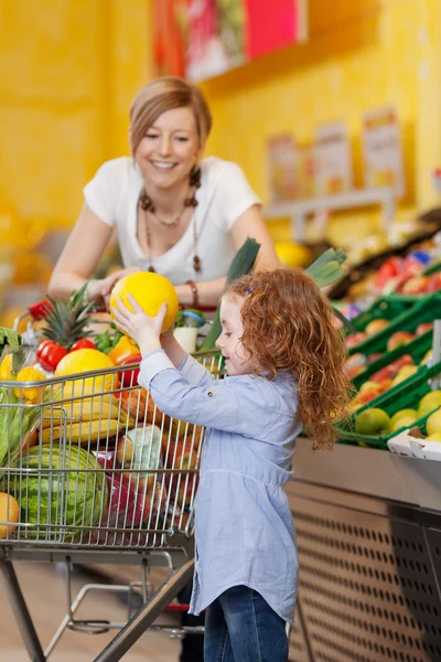 Mädchen hält Muskmelone im Einkaufswagen, während Mutter anschaut — Stockfoto