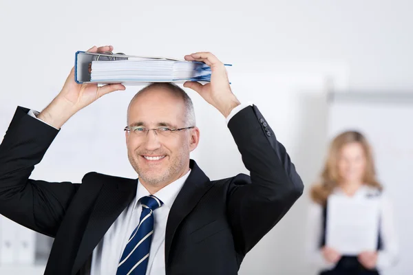 Smiling businessman holds a binder on his head — Stock Photo, Image