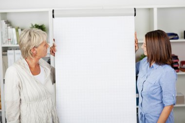 Two women looking at the flipchart in office clipart