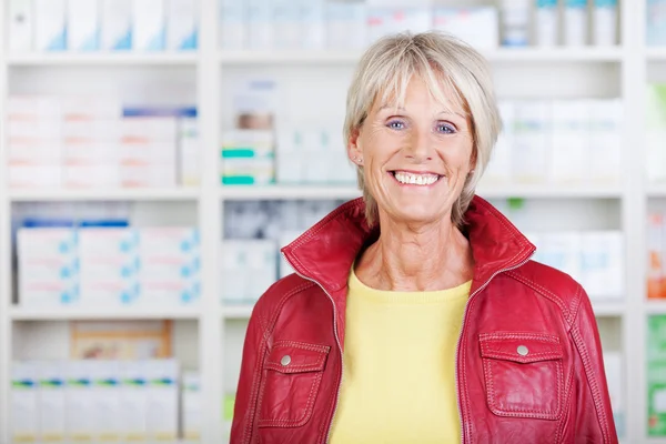 Farmacêutica feminina vestindo jaqueta enquanto sorri na farmácia — Fotografia de Stock