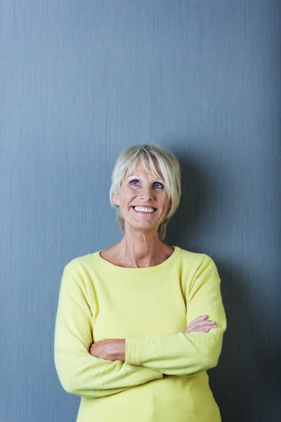 Seniorin mit verschränkten Armen blickt gegen blaue Wand — Stockfoto