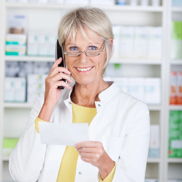 Farmacista che utilizza il telefono cordless mentre tiene carta di prescrizione — Foto Stock