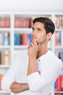 Student With Hand On Chin Looking Away In Library clipart