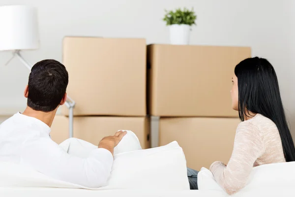 Casal inclinado no sofá com caixas de papelão no fundo — Fotografia de Stock