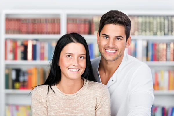 Happy couple standing in front of the bookshelf — Stock Photo, Image