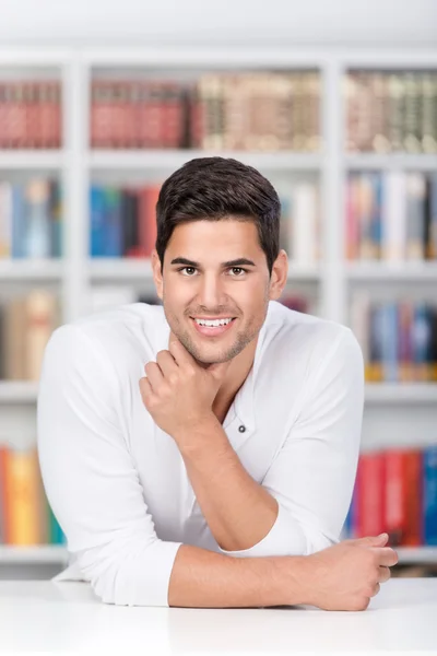 Estudiante masculino apoyado en el escritorio en la biblioteca —  Fotos de Stock