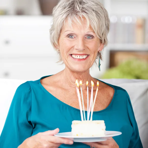 Senior mulher segurando bolo de aniversário com velas de lit em casa — Fotografia de Stock