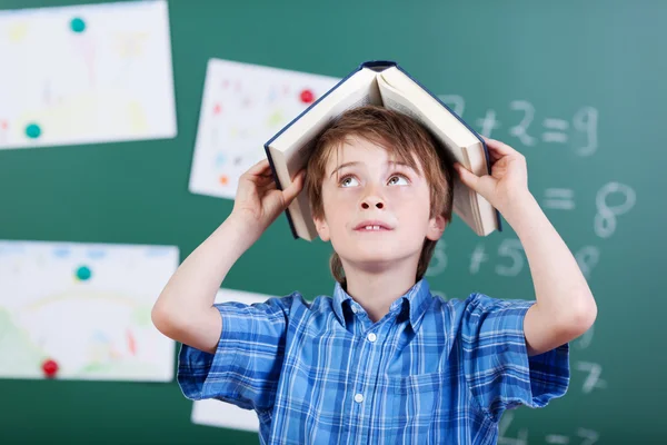 Joven estudiante de primaria con un libro sobre la cabeza — Foto de Stock