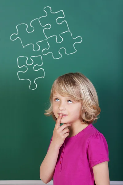 Puzzled schoolgirl in front of the blackboard — Stock Photo, Image