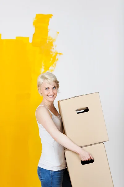 Mulher carregando caixas de papelão contra metade da parede pintada de amarelo — Fotografia de Stock