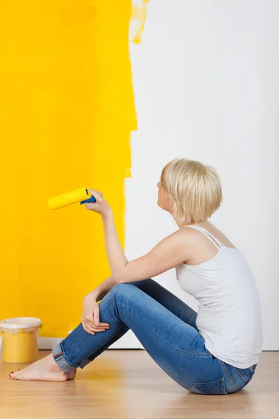Kvinna med paint roller tittar på gula väggen — Stockfoto